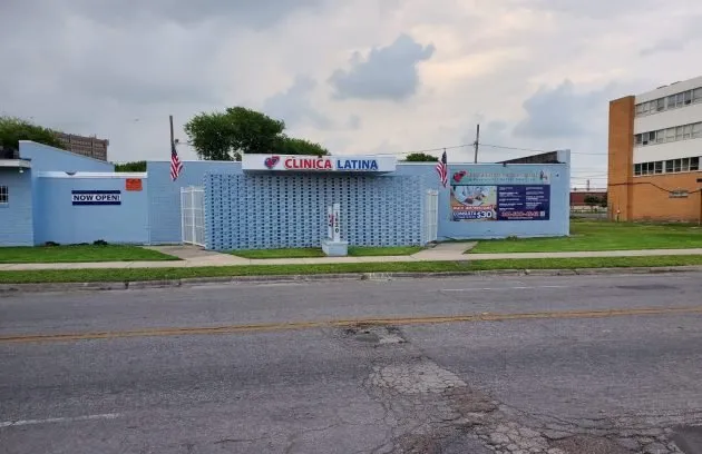View of the Clínica Latina Corpus Christi storefront from the street, with the sign and flags
